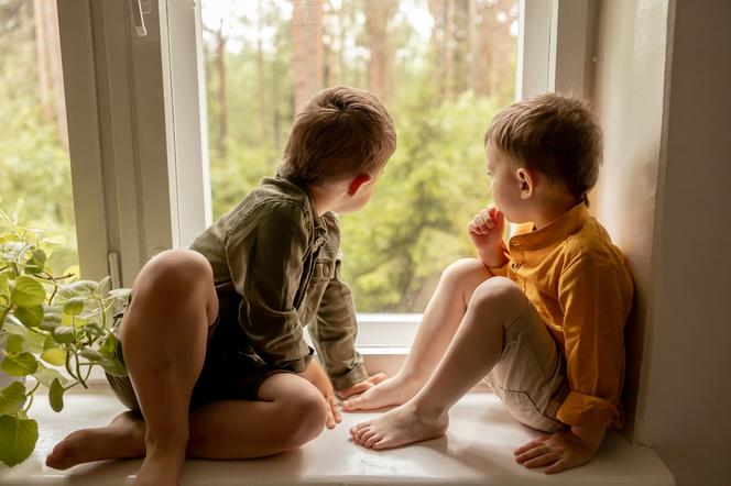dwóch chłopców siedzących na parapecie i wyglądających przez okno 