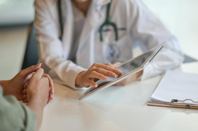 Ujęcie lekarza pokazującego pacjentowi wyniki badań na tablecie cyfrowym. 