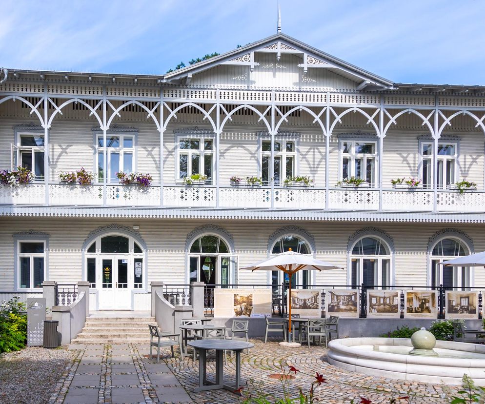 Odrestaurowany Pensjonat Gurewicza w Otwocku, o fasadzie w stylu świdermajer z bogato zdobionymi werandami, balkony z kwiatami i drewnianą elewacją. Przed nim kamienny dziedziniec z meblami ogrodowymi i fontanną. Więcej o renowacji na Architektura Murator Plus.