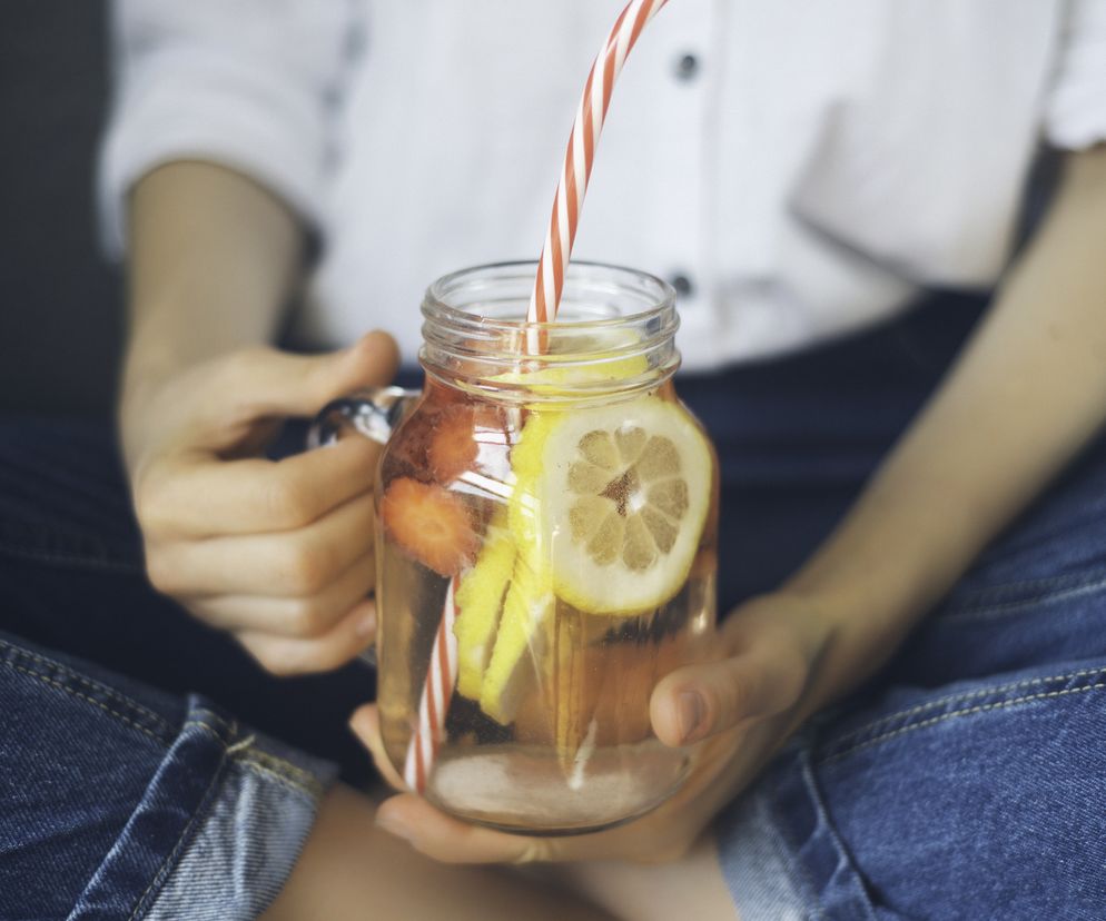 Kobieta siedzi po turecku i trzyma w ręce szklankę z wodą ze świeżymi owocami.