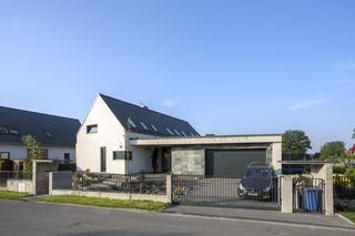 Dwie bryły. Od frontu na mieszkalną wygląda jedynie część bryły pod dwuspadowym dachem – nawiązująca do tradycyjnego kształtu domu. Już wkrótce sąsiadujący z nią płaski dach – taras porośnie trawa, która ożywi oszczędną, minimalistyczną architekturę