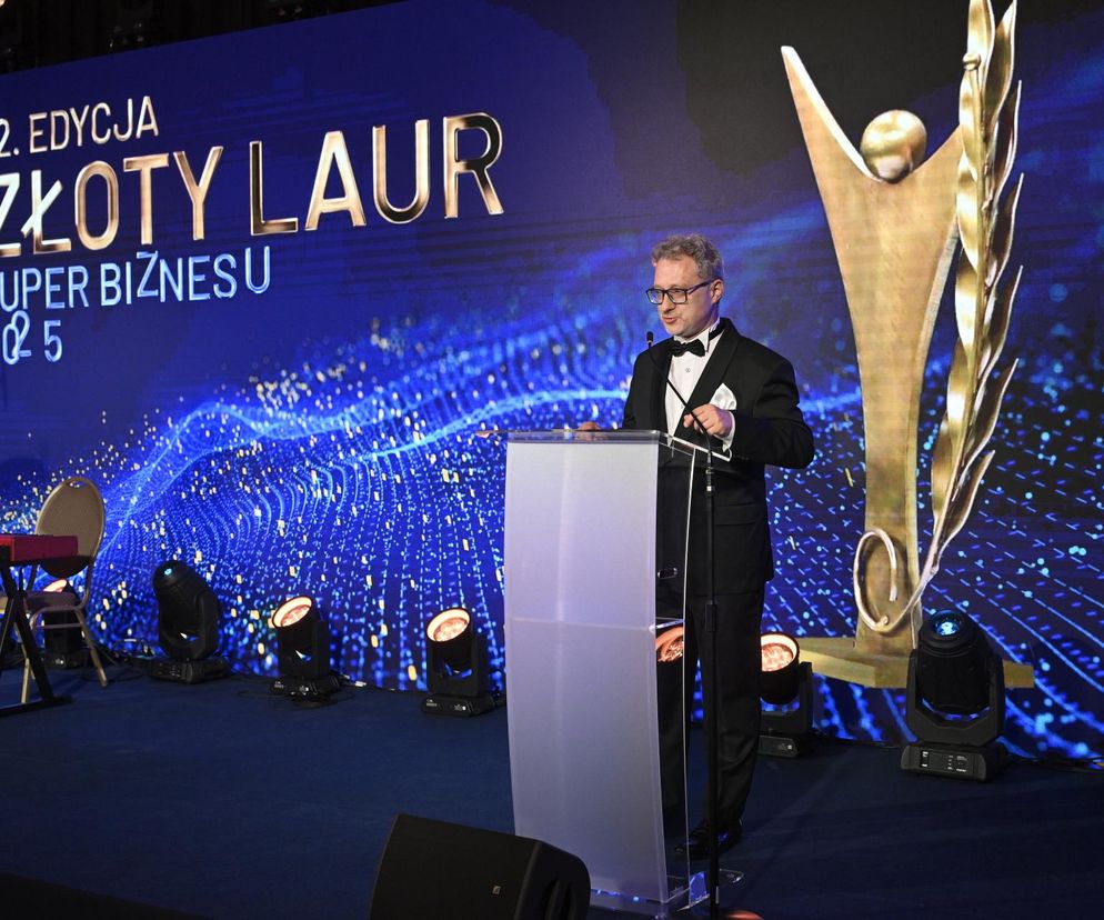 Mężczyzna w smokingu przemawia z mównicy, obok widoczna duża statuetka Złotego Lauru. W tle ekran z napisem 12. Edycja Złoty Laur Super Biznesu 2025. Zdjęcie przedstawia uroczystość wręczenia nagród, o których można przeczytać na portalu Super Biznes.