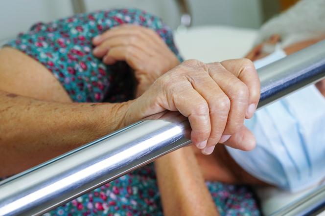 Starsza kobieta trzyma poręcz szpitalnego łóżka