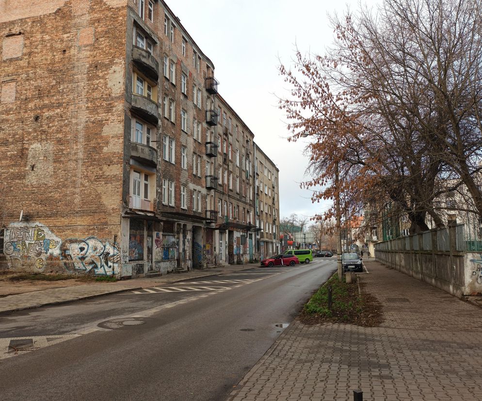 Ulica Środkowa w Warszawie przed przebudową, z widocznymi zniszczonymi kamienicami z cegły, graffiti na parterze i parkującymi samochodami. Drzewa bez liści i zaniedbane pobocze oddają obecny stan. O zmianach na Pradze-Północ przeczytasz na Architektura Murator Plus.