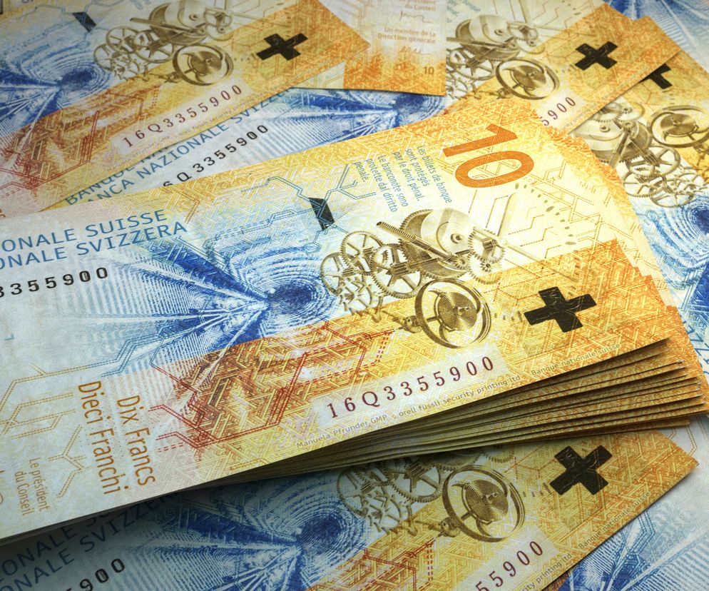 Banknoty franków szwajcarskich, w tym ułożone w plik i rozłożone, z widocznymi nominałami 10 franków, symbolami plusa oraz mechanizmem zegarowym, symbolizujące stabilność waluty. Więcej o kursach walut na Super Biznes.