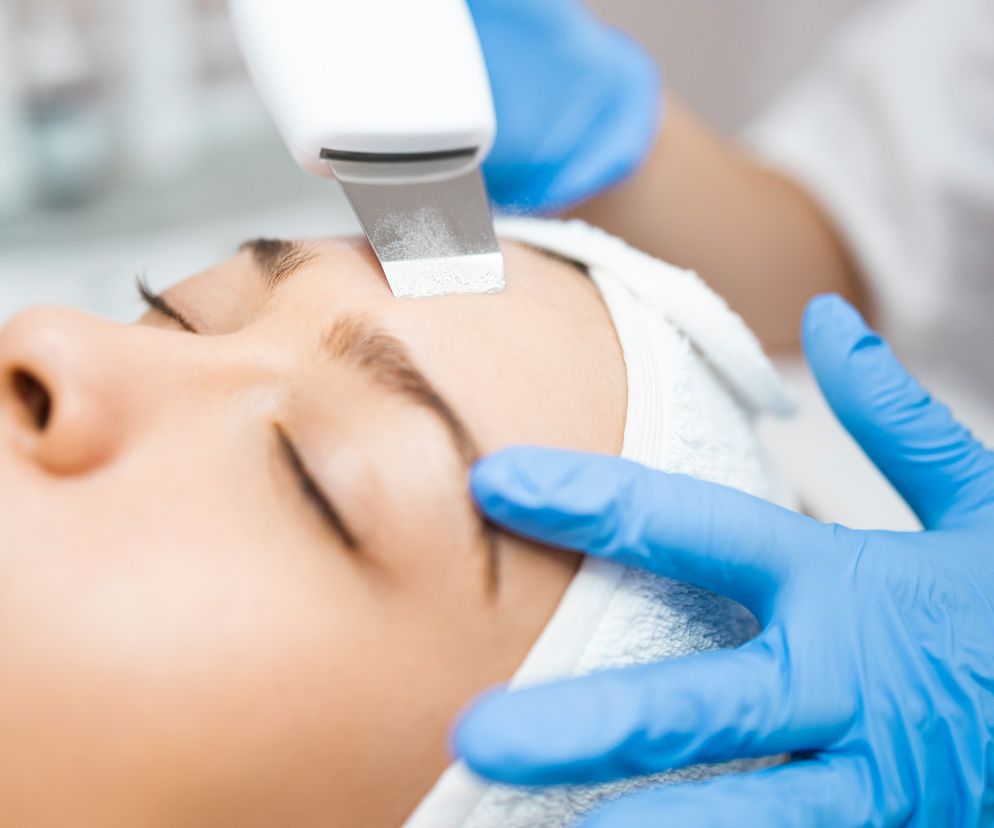 Kosmetyczka wykonuje peeling kawitacyjny za pomocą specjalnej szpatułki emitującej fale ultradźwiękowe. Zabieg w salonie kosmetyczym.