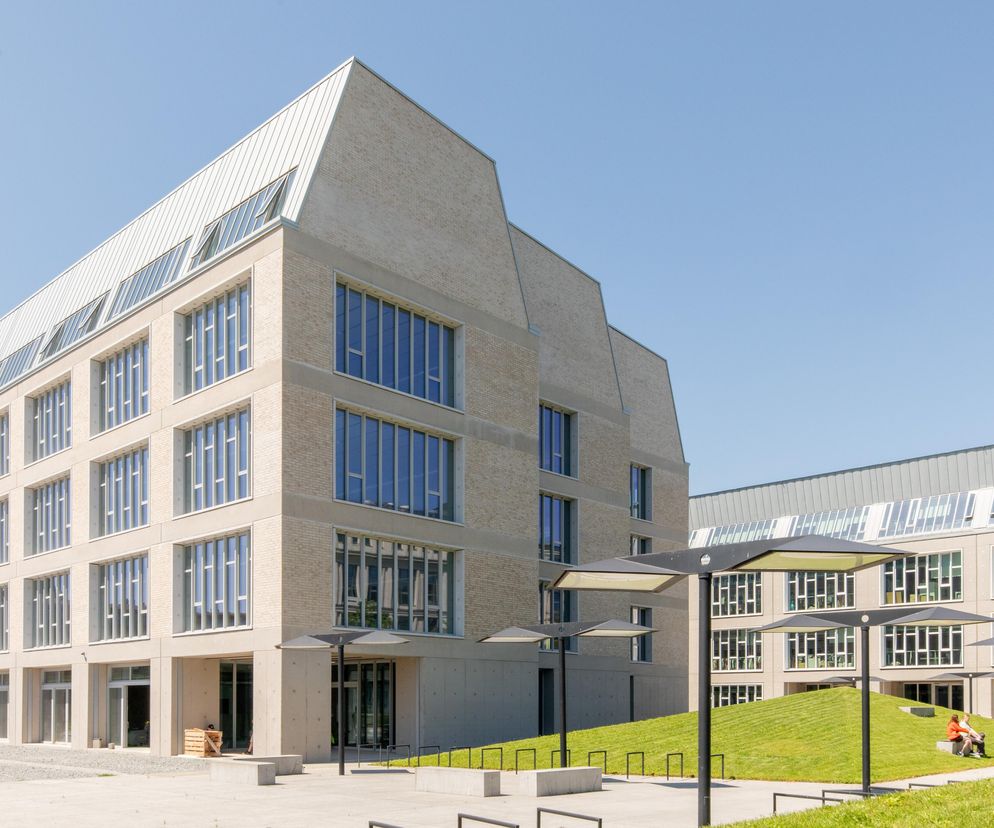 Nowoczesne budynki LPP Fashion Lab autorstwa JEMS Architekci, z jasnej cegły, z charakterystycznymi spadzistymi dachami i dużymi oknami, otoczone zielonymi pagórkami i parasolami, tworzą przestrzeń, o której można przeczytać na Architektura Murator Plus.