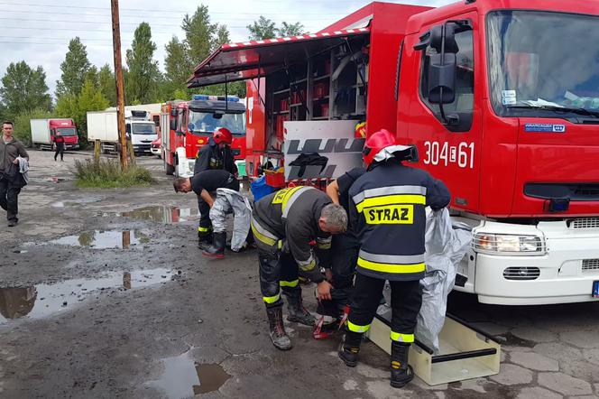 Na miejscu jest 5 wozów strażackich. Strażacy w kombinezonach i maskach gazowych neutralizują kwas