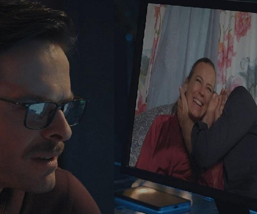 Adrian Budakow jako Błażej Święcicki w okularach, z wąsami, podglądający na laptopie Annę Muchę jako Magdę Budzyńską z Krystianem Wieczorkiem jako Andrzejem Budzyńskim. Ona, w czerwonej koszuli, śmieje się, obejmowana. Scena z serialu M jak miłość, więcej na Super Seriale.