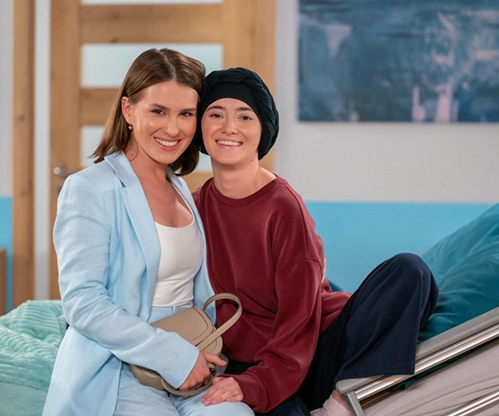 Aktorki Patrycja Franczak (Angelika) w czarnej chuście i Anna-Maria Sieklucka (Eliza) w błękitnym komplecie, uśmiechnięte, razem w szpitalu, symbolizując powrót do zdrowia Angeliki w serialu Pierwsza miłość. Więcej o losach bohaterów przeczytasz na stronie Super Seriale.