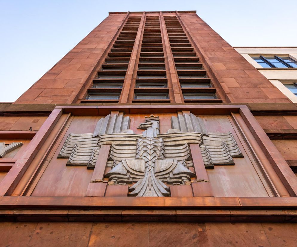 Polski orzeł w stylu art déco, umieszczony na fasadzie dawnego Ministerstwa Oświaty Publicznej w Warszawie, dzieło rzeźbiarza Karola Tchorka. Ten monumentalny symbol II RP, przedstawiony na tle czerwono-brązowej elewacji, jest przykładem wyjątkowych dzieł architektury, o których przeczytasz na portalu Architektura Murator Plus.