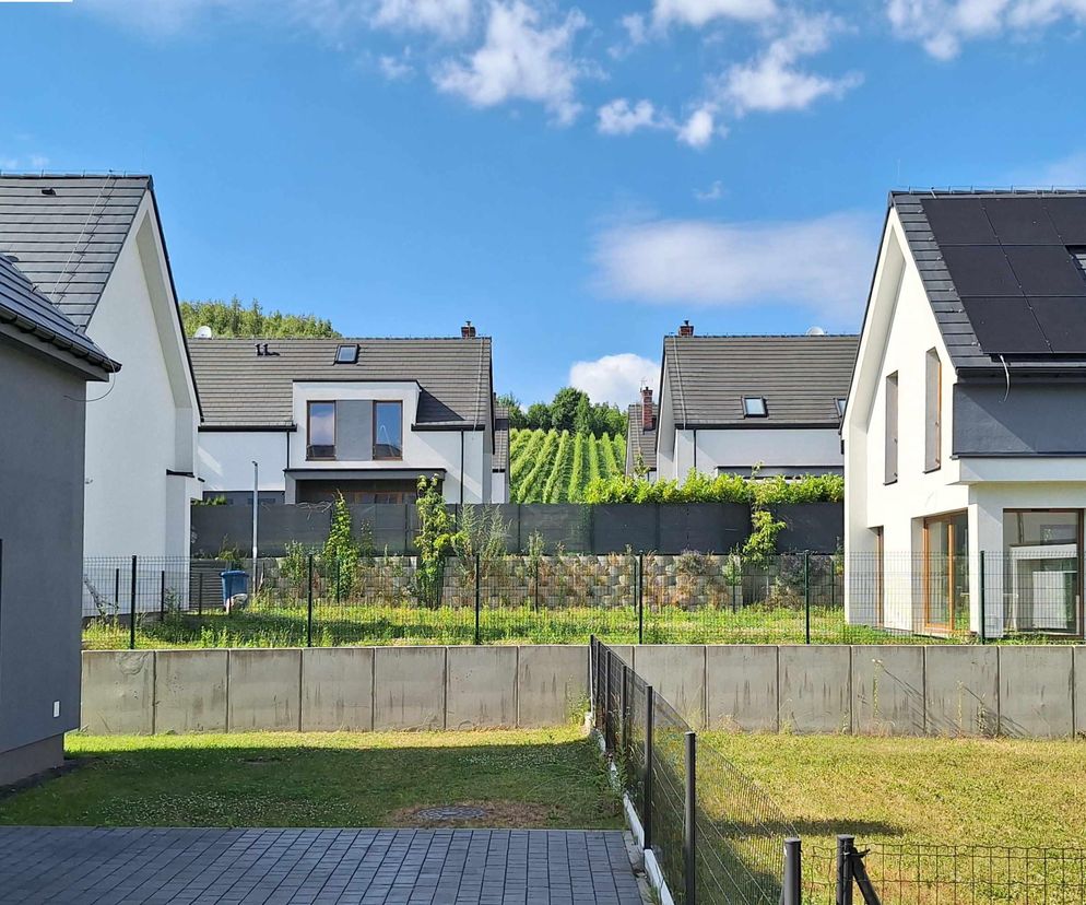 Nowoczesne domy jednorodzinne na Osiedlu Tyniec Park, w stonowanej kolorystyce bieli i szarości, z ciemnymi dachami i oknami dachowymi, otoczone zielenią, nawiązują do walorów współczesnej architektury i ducha miejsca, o czym przeczytasz na Architektura Murator Plus.