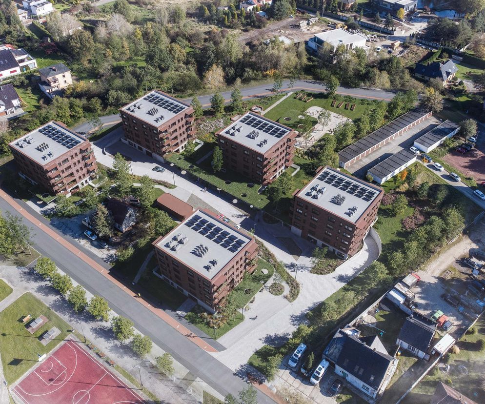 Widok z lotu ptaka na nowe osiedle w Gliwicach z brązowymi budynkami wielorodzinnymi, zielonymi terenami i infrastrukturą, w tym boiskiem sportowym. To zwycięski projekt konkursu SARP, o którym przeczytasz na Architektura Murator Plus.