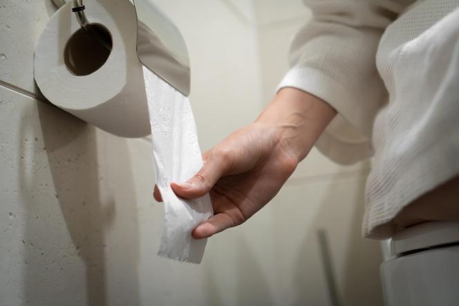 kobieta wyciaga rękę po papier toaletowy