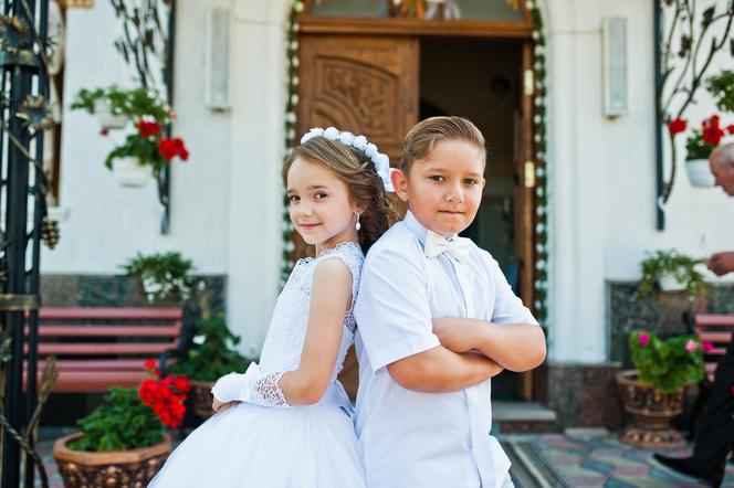 Chłopiec i dziewczynka ubrani w komunijne szaty pozują do zdjęcia