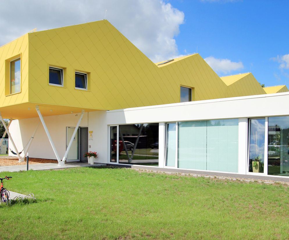 Nowoczesne Publiczne Przedszkole nr 6 KIDO w Aleksandrowie Łódzkim, autorstwa pracowni xystudio, charakteryzuje się dynamiczną formą z żółtym piętrem wspartym na skośnych słupach, częścią parterową z dużymi przeszkleniami oraz zielonym trawnikiem. Obiekt, zgłoszony do konkursu Życie w Architekturze, promuje energooszczędność, o czym przeczytasz więcej na Architektura Murator Plus.