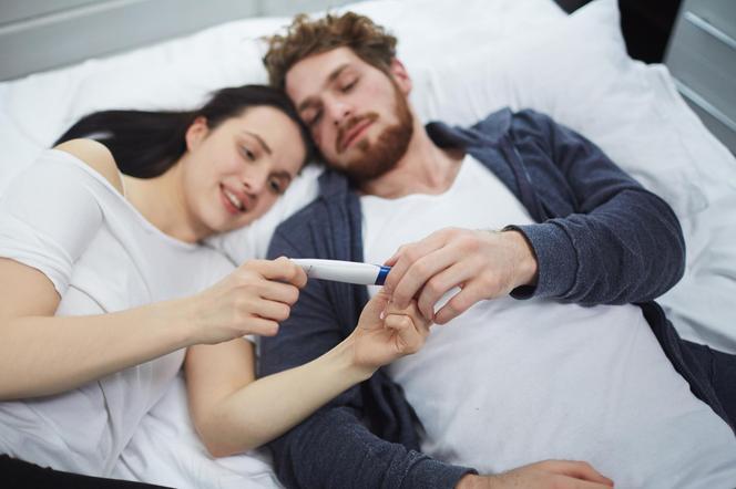 Para leżąca w łóżku i patrząca na test ciążowy