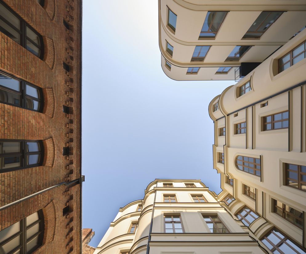 Ujęcie Rezydencji Emilii Plater w Warszawie, łączące zabytkową ceglaną fasadę kamienicy Wittów z nowoczesną, beżową zabudową mieszkalną, wyróżnia się dbałością o detale, takie jak ażurowe przesłony inspirowane balustradami, o czym szerzej można przeczytać na Architektura Murator Plus.