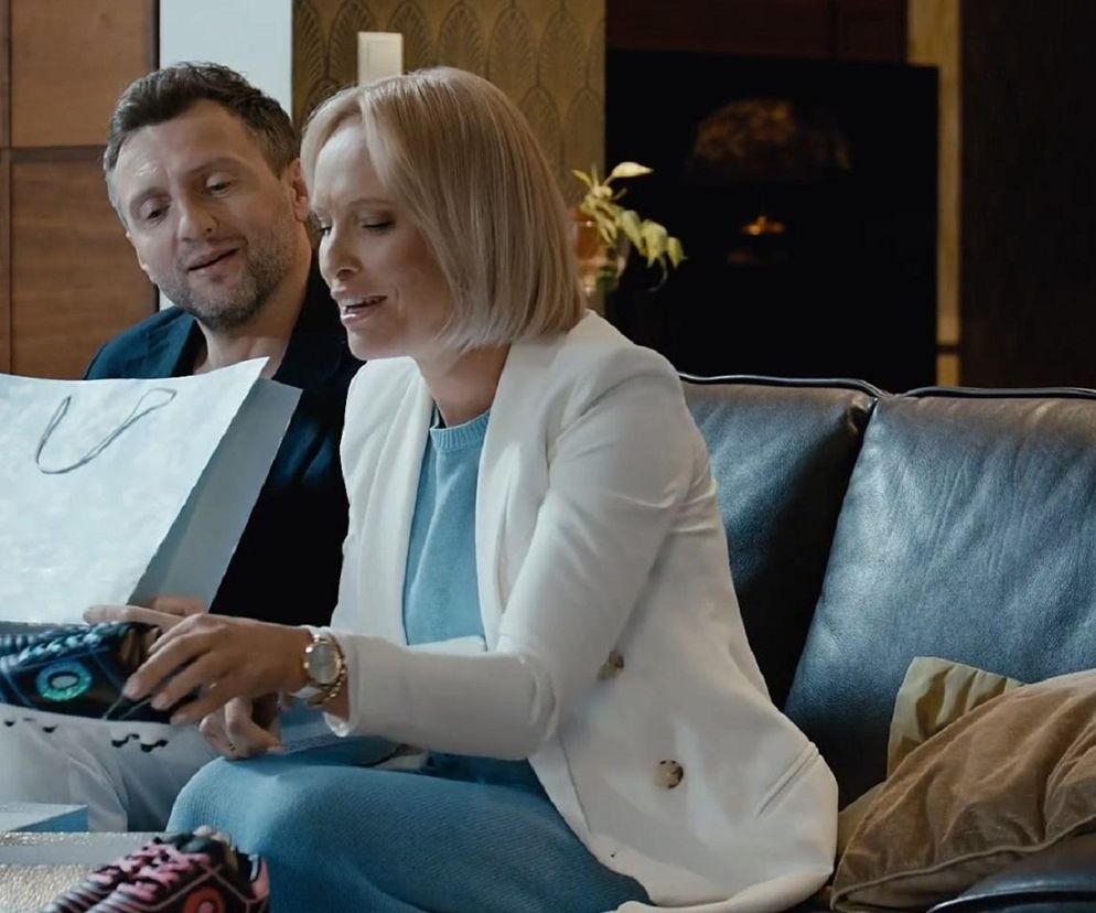 Dorota i Bartek z M jak miłość siedzą na kanapie; Bartek trzyma torebkę prezentową, a Dorota ogląda wyjęte z niej czarne buty sportowe z zielono-niebieskimi elementami. Jest to prezent dla ich przyszłego syna, o czym można przeczytać na Super Seriale.