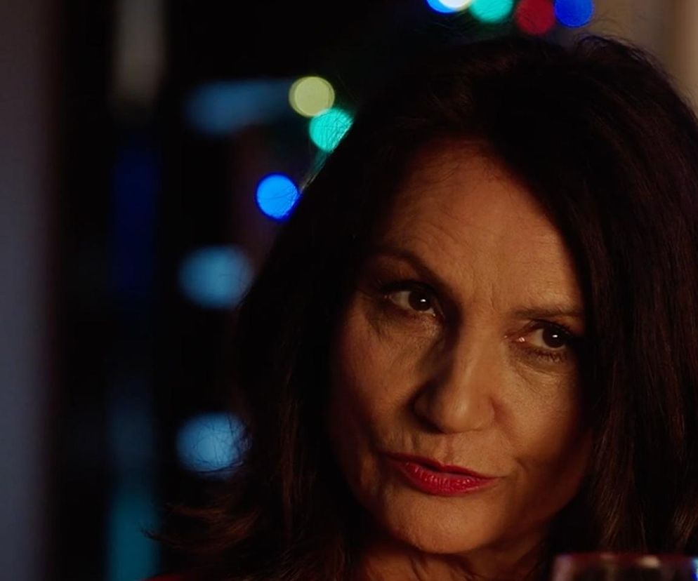 Portret aktorki Małgorzaty Pieczyńskiej jako Aleksandry z serialu M jak miłość. Ma ciemne włosy, brązowe oczy i pomalowane na czerwono usta. Za nią widać rozmyte, kolorowe światła. Więcej informacji o serialu znajdziesz na Super Seriale.