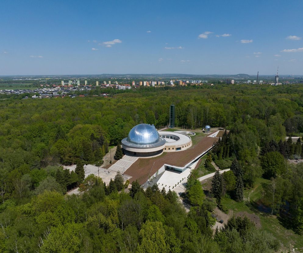 Widok z lotu ptaka na Planetarium Śląskie w Chorzowie, przedstawiający główną kopułę, obserwatorium i łączący je pierścień. Obiekt, otoczony bujną zielenią Parku Śląskiego, harmonijnie wtapia się w krajobraz, co można podziwiać na Architektura Murator Plus.
