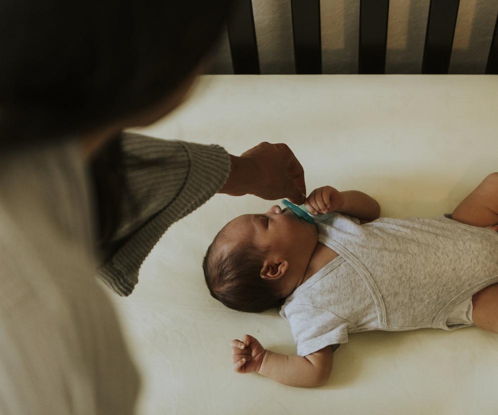 mama wyjmująca śpiącemu niemowlęciu smoczka z buzi