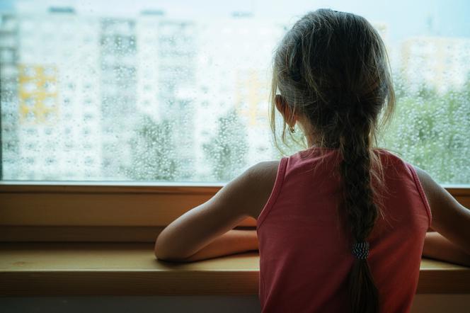 Smutna dziewczynka patrzy przez okno