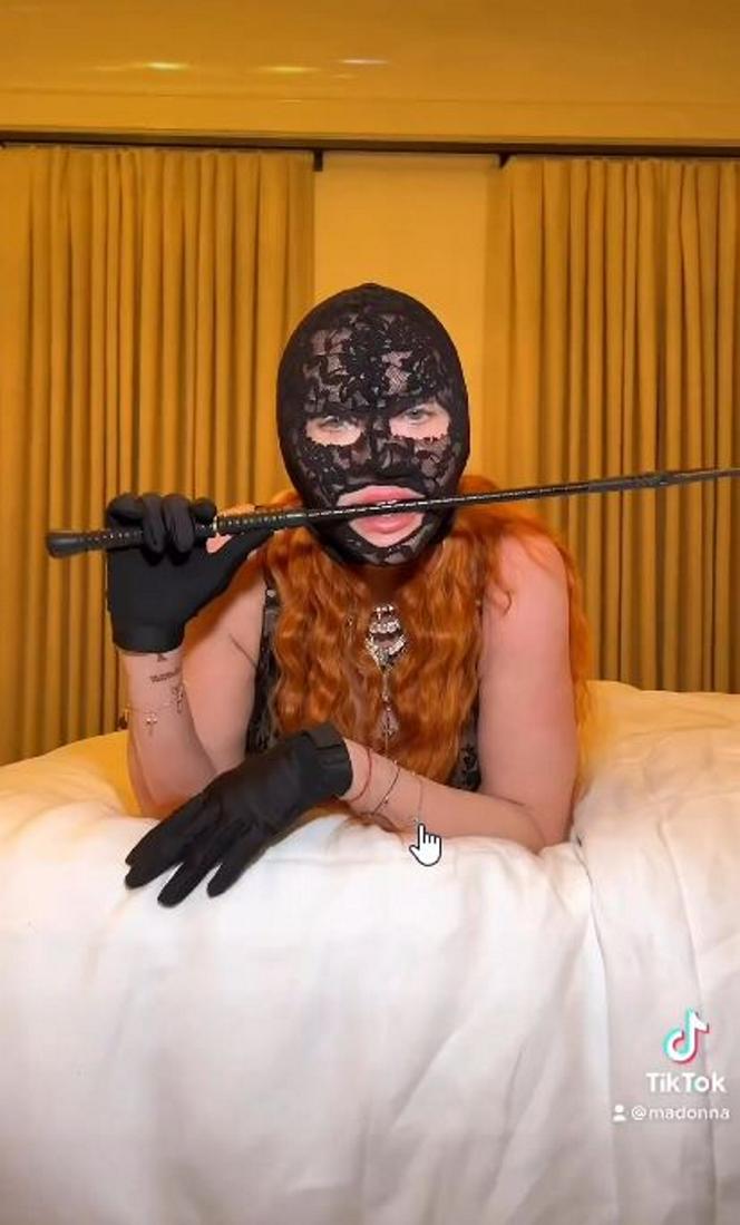 Madonna w kominiarce rzuca się w konwulsjach po łóżku. W ręce trzyma pejcz. "Ocknij się kobieto"