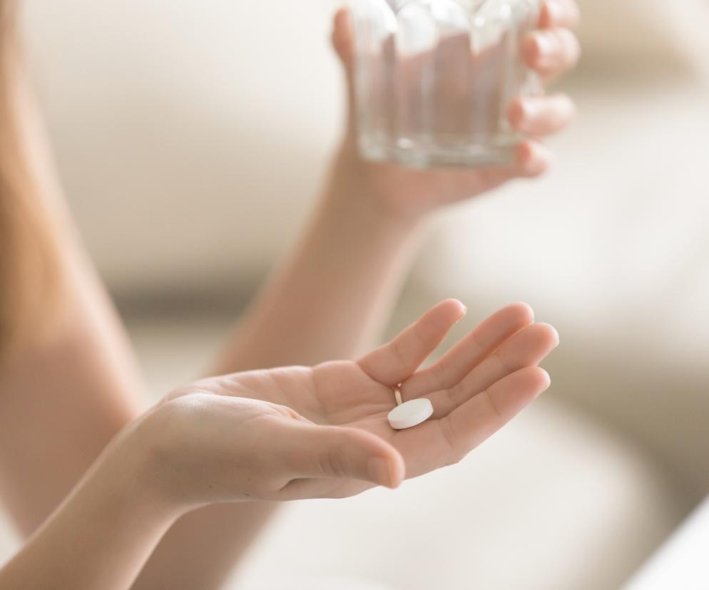 Kobieta trzyma w dłoni białą tabletkę