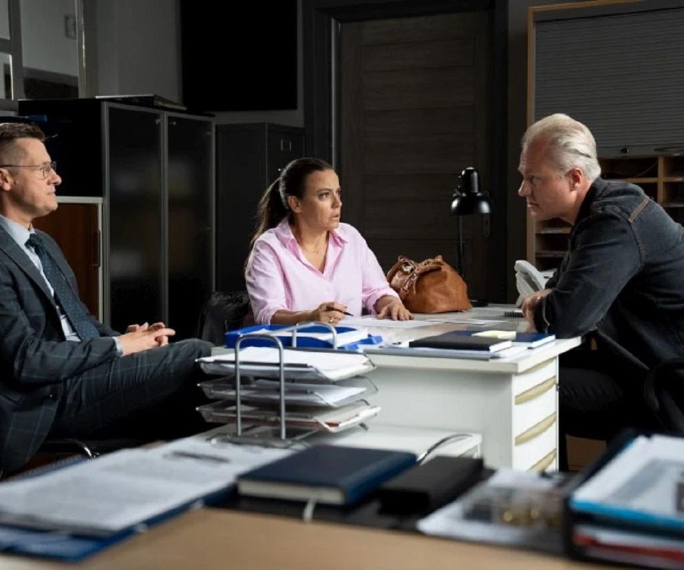 Piotrek Zduński (Marcin Mroczek) w eleganckim garniturze, Magda Budzyńska (Anna Mucha) w różowej koszuli i aspirant Przewrocki (Remigiusz Jankowski) podczas przesłuchania na komisariacie, co wiąże się z intrygą hakerów z serialu M jak miłość. Więcej o losach Magdy na Super Seriale.