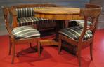 Biedermeier. Salonik w formach wczesnego biedermeieru – w kształtach krzeseł widoczne wpływy tradycji klasycystycznej. Charakterystyczna podpora stołu (kolumna oparta na trójnożnej podstawie). 