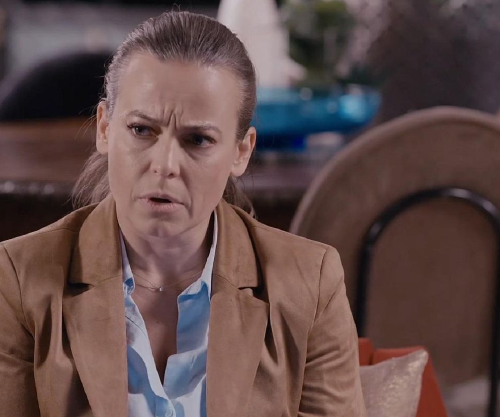 Anna Mucha jako Magda Budzyńska z M jak miłość z poważną miną w jasnobrązowej marynarce i błękitnej koszuli. Jej włosy są związane w kok, a na szyi ma delikatny naszyjnik. Na portalu Super Seriale przeczytasz o podstępie Święcickiego.