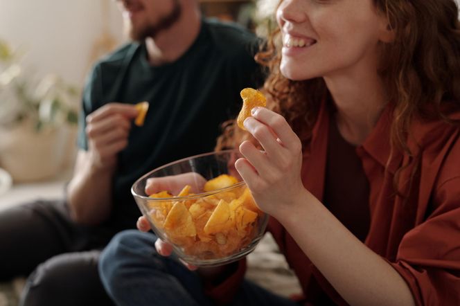 Kobieta i mężczyzna jedzą chipsy. Śmieciowe jedzenie