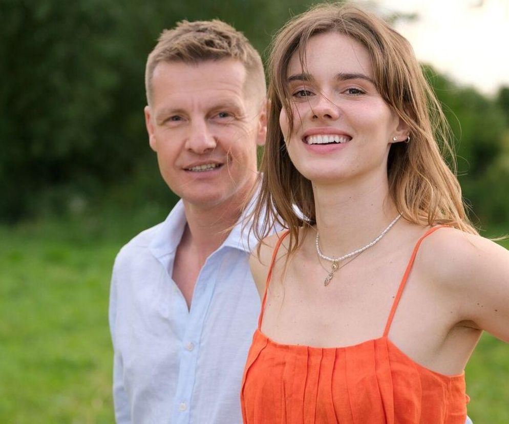 Uśmiechnięta Dominika Kachlik jako Franka w pomarańczowej sukience i Rafał Mroczek jako Paweł w jasnoniebieskiej koszuli na tle zielonej łąki, para znana z serialu M jak miłość. Więcej informacji o ich losach znajdziesz na Super Seriale.