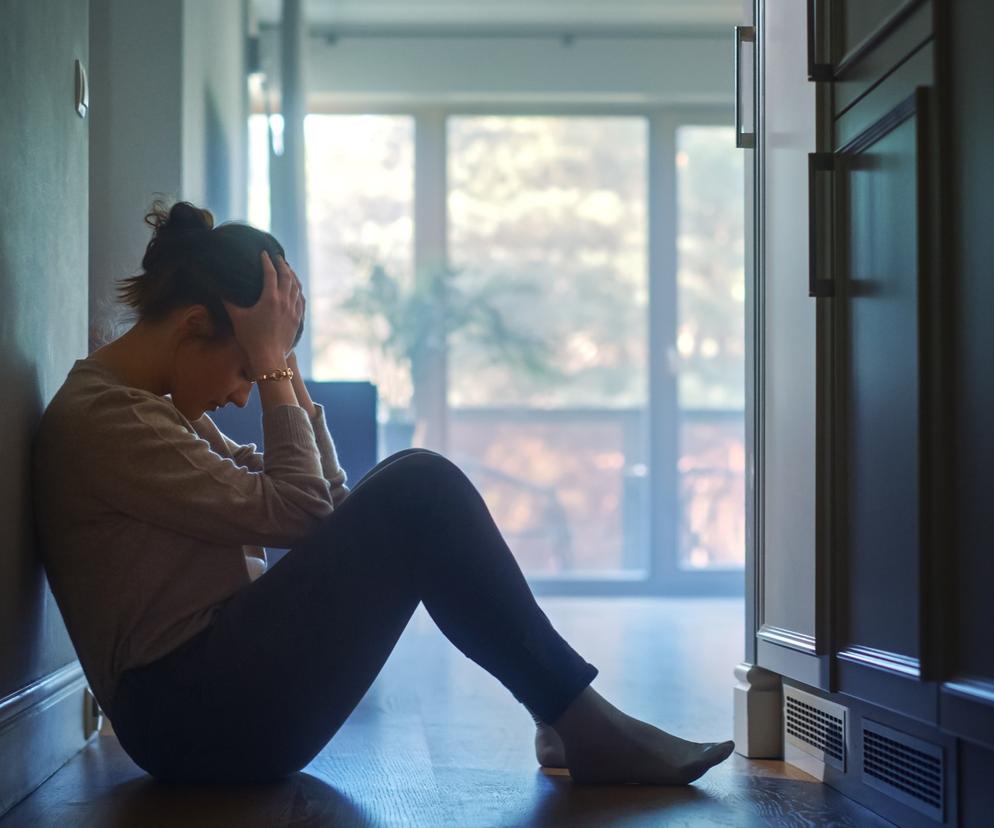 Smutna kobieta siedzi na podłodze przy ścianie 