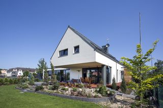 Lewitujące poddasze. Widok na część wypoczynkową od ogrodu z zacienionym fragmentem tarasu pod częścią poddasza