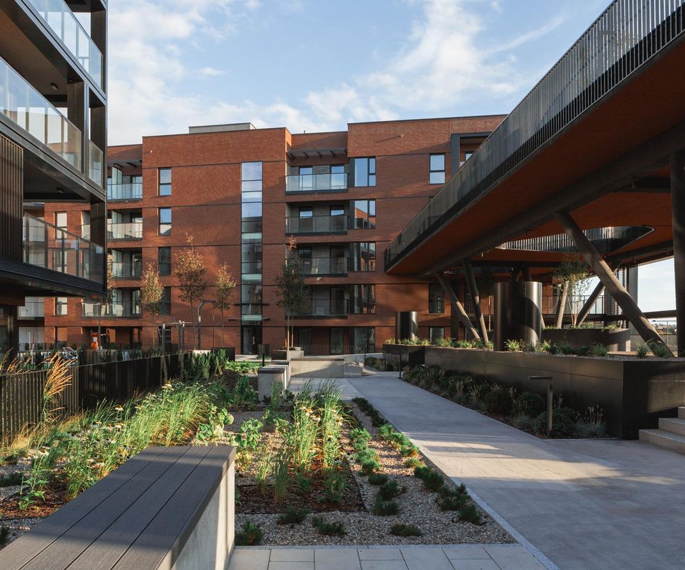 Nowoczesny kompleks Nadmotławie Apartments w Gdańsku autorstwa SIM Architekci, z ceglanymi elewacjami i szklanymi balkonami, otoczony zielonym patio z ławkami i ścieżkami, z charakterystyczną ażurową konstrukcją mostową. Więcej o tym na Architektura Murator Plus.