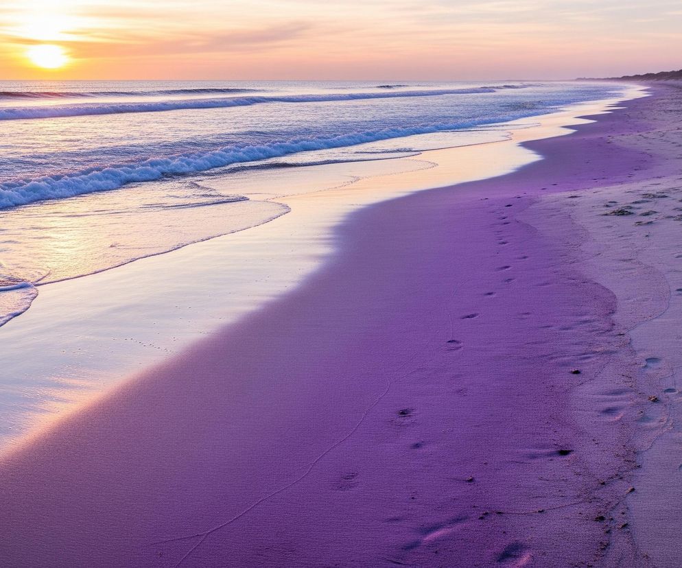 Plaża oświetlona zachodzącym słońcem rozciąga się wzdłuż linii brzegowej. Falująca woda morza, z białymi grzywami, odbija pomarańczowe i fioletowe odcienie nieba. Piasek na pierwszym planie jest zabarwiony intensywnym fioletem, a liczne ślady stóp widoczne są na jego powierzchni, prowadząc w głąb obrazu, gdzie przechodzi w bardziej naturalny, beżowy kolor. Na horyzoncie, po prawej stronie, widać wydmy pokryte trawą, a nad nimi rozpościera się niebo z ciepłymi barwami zachodzącego słońca.
