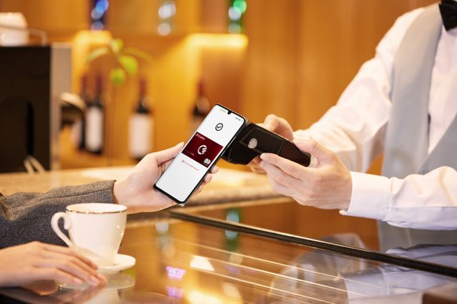Osoba płacąca zbliżeniowo smartfonem Samsung, którego ekran wyświetla kartę płatniczą Curve z logo Mastercard, podczas gdy kelner obsługuje terminal płatniczy. Scena podkreśla wygodę nowoczesnych płatności mobilnych, o których więcej dowiesz się na Super Biznes.