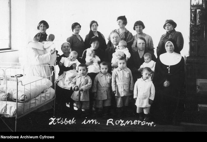 Fotografia grupowa dzieci i opiekunek z fundatorem żłobka Kazimierzem Rosnerem. Widoczne m.in. panie z komitetu zarządzającego i kierowniczka żłobka p. Sozańska (siedzi 5. z prawej); 1921 - 1939.