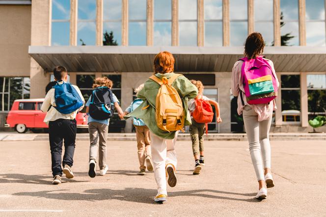dzieci biegnące do szkoły z plecakami
