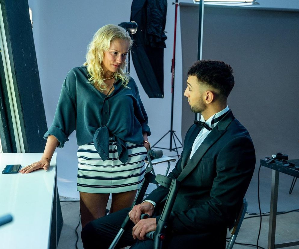 Sylwia Juszczak-Krawczyk jako Justyna Zytko i Oliwier Kozłowski jako Mirek na planie Barw szczęścia. Aktor siedzi w eleganckim garniturze z muszką i opiera ręce o kule, kobieta patrzy na niego. Więcej o ich losach przeczytasz na portalu Super Seriale.