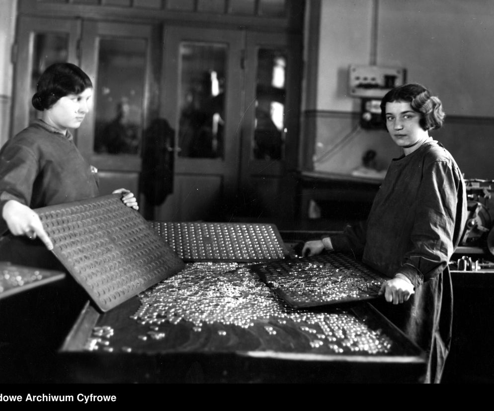 Dwie kobiety w Mennicy Państwowej sortują monety na tackach. Fotografia z lat 1924-1926 z Narodowego Archiwum Cyfrowego, ilustrująca historię polskiej waluty. Więcej o historii złotego przeczytasz na Super Biznes.