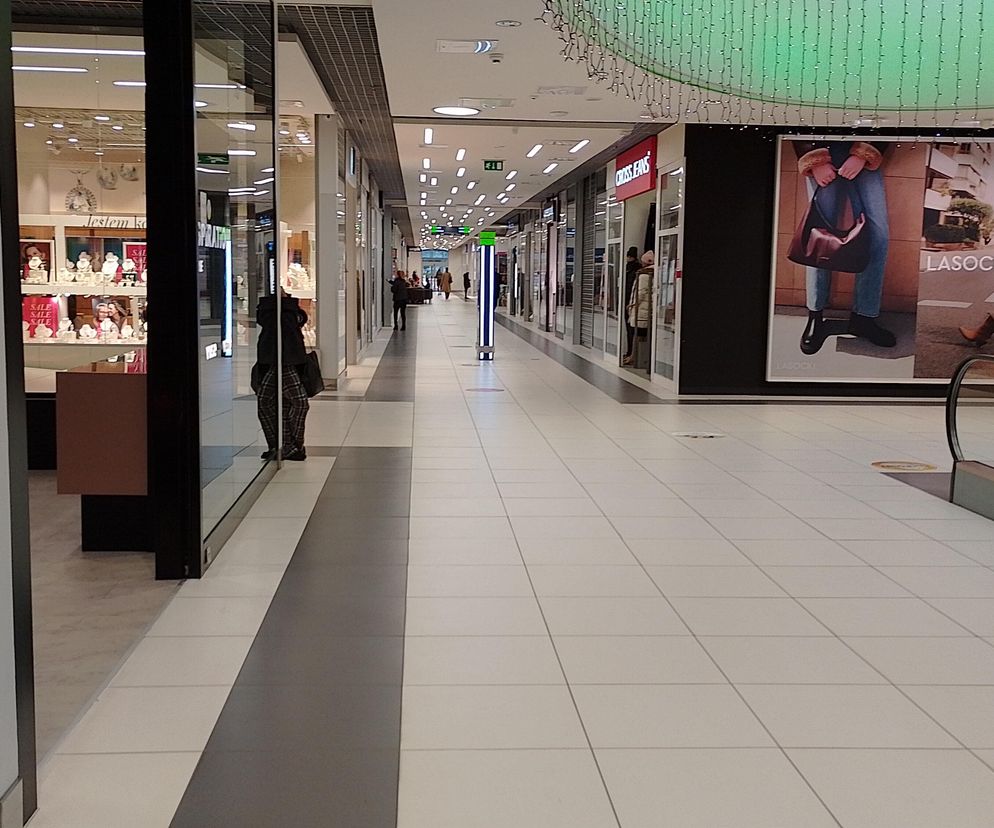 Pusty korytarz centrum handlowego z zamkniętymi sklepami i kilkoma sylwetkami ludzi w oddali, symbolizujący zakaz handlu w niedziele. Na reklamie widoczne logo CCC. O niedzielach handlowych w 2026 roku przeczytasz na portalu Super Biznes.