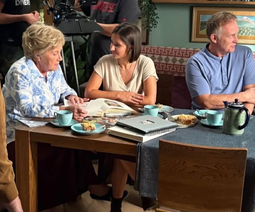 Ujęcie z planu M jak miłość, gdzie Barbara Mostowiakowa, grana przez Teresę Lipowską, i Artur Rogowski (Robert Moskwa) siedzą przy stole z Agnes (Amanda Mincewicz). Na stole kubki, imbryk i ciastka. Scena z serialu o gościnności i rodzących się problemach, o których czytasz na Super Seriale.