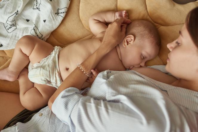 kobieta leżąca w łóżku i karmiąca piersią niemowlę