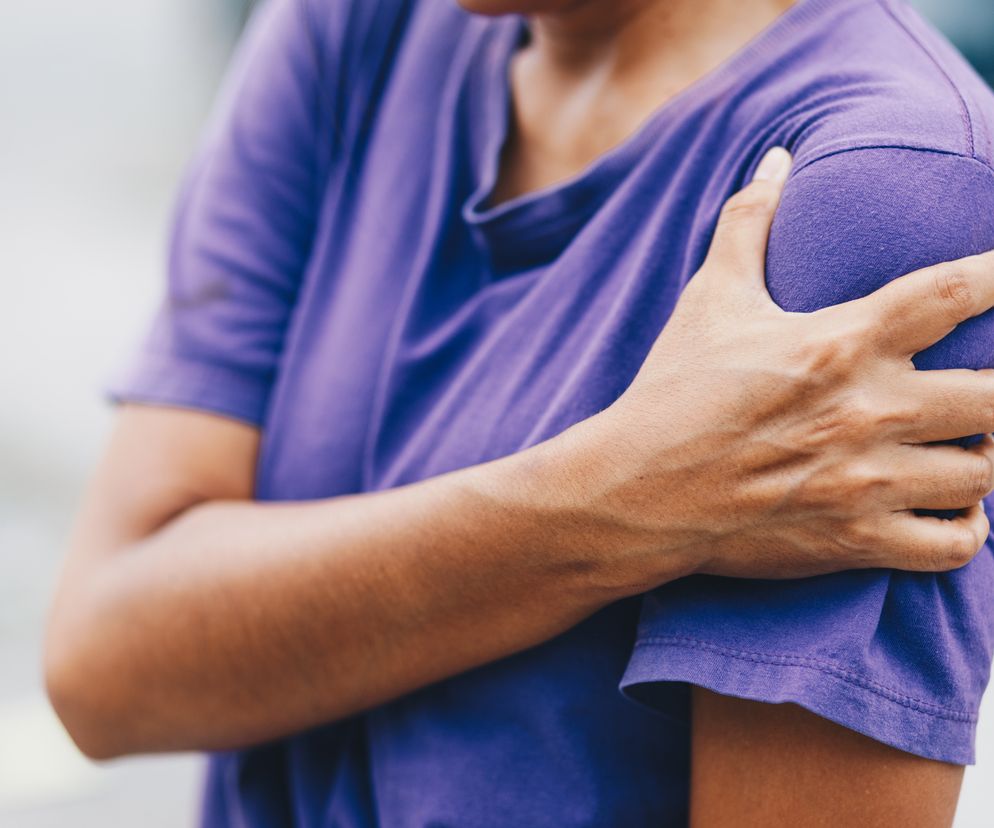 Mężczyzna trzymający się za bolący lewy bark.