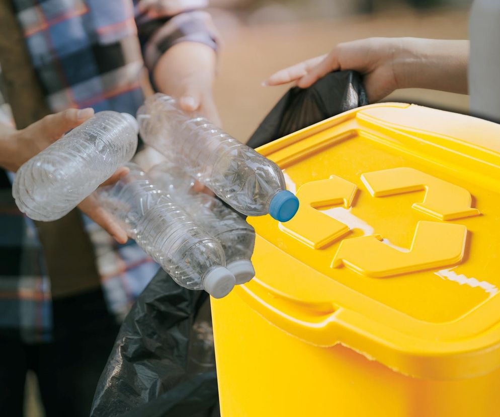 Osoba wrzucająca plastikowe butelki do żółtego pojemnika z symbolem recyklingu. Zdjęcie ilustruje zmiany w systemie kaucyjnym i zasady segregacji odpadów, o których można przeczytać na portalu Super Biznes.