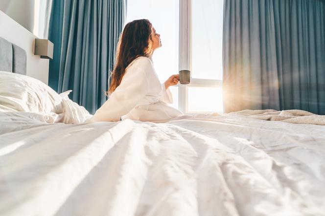 Kobieta siedzi na łóżku z poranną kawą