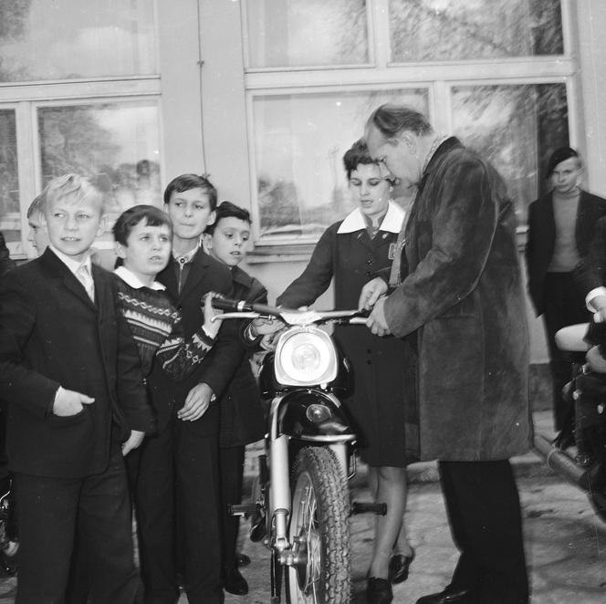 Grupa chłopców w towarzystwie pracowników wystawy ogląda motorower przed budynkiem Powiatowego Domu Kultury, 1968